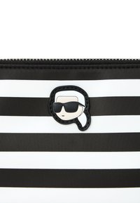 Pochette rayée noir et blanc avec une fermeture éclair, ornée d'un visage noir et blanc au style cartoon portant des lunettes de soleil comme détail principal.