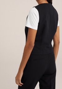 Czarna, dopasowana kamizelka o zorganizowanej konstrukcji, zestawiona z białą koszulą z krótkim rękawem, prezentującą gładką teksturę i minimalistyczny styl.
