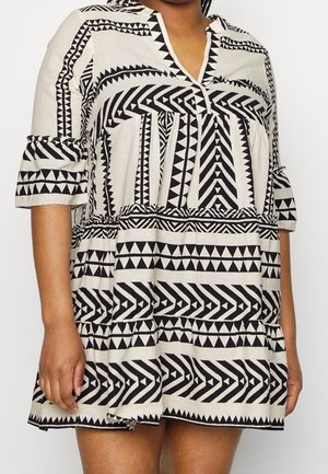 Vrouw die een korte, loszittende zwart-witte jurk draagt met geometrische tribale patronen en driekwart mouwen.