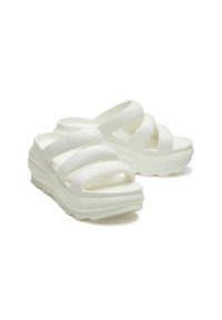 Weiße, geformte Plattform-Sandalen mit drei breiten, weichen Riemen und einer strukturierten Sohle, die eine glatte Oberfläche und eine konturierte Form aufweisen.