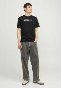 Zwarte katoenen t-shirt met korte mouwen, voorzien van het "JACK & JONES" logo in het wit. Gecombineerd met losse, vervaagde grijze jeans en casual schoenen.