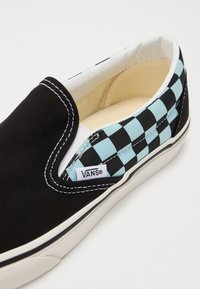 Juoda slip-on Vans avalynė su šachmatų raštu šviesiai mėlynos ir juodos spalvos. Kanvoso medžiaga su balta siūle ir guma padu.