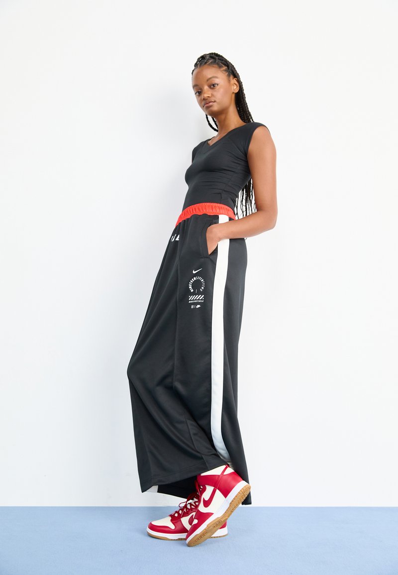 Pantalones deportivos negros con cinturilla elástica roja, franjas laterales blancas y un detalle de logo; combinados con zapatillas altas rojas de Nike.