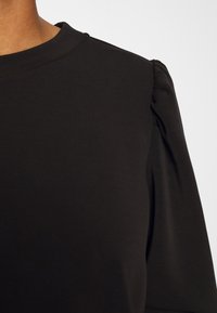 Black short-sleeve top with a rounded neckline and puffed shoulders, made of smooth, soft fabric. Minimalist design with subtle texture.