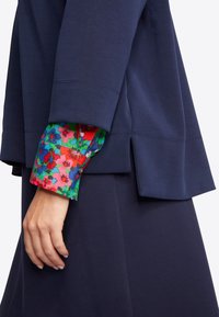 Navyblaues Oberteil mit einem blumigen, farbenfrohen Bündchen. Es hat eine lockere Passform und seitliche Schlitzöffnungen für Bewegungsfreiheit.