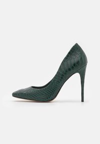 Pompe stiletto à talon haut en vert foncé avec une texture crocodile brillante, un bout pointu et un talon fin sur fond blanc.