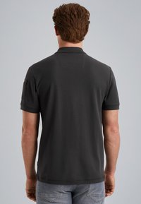 Donkergrijze polo met korte mouwen, platte kraag en een klein vakje op de linkerschouder. Gladde stoftextuur, casual ontwerp.