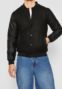 Svart bomberjacka med ullkropp och läderärmar, knappstängning, ribbade cuffs och sidofickor. Stylen är kompletterad med blå jeans.