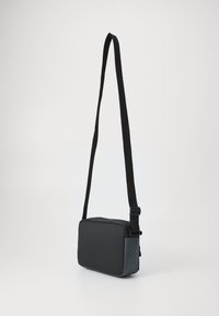 Čierna obdĺžniková crossbody taška s nastaviteľným popruhom, vyrobená z hladkého materiálu, s bočným zipsovým vreckom a elegantným dizajnom.