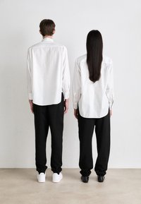 Hvite, knappede skjorter med avslappet passform, brukt med svarte bukser. Lange ermer, skjortene er litt lengre bak. Sko: hvite joggesko og svarte hæler.