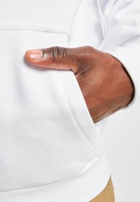 Hvid hoodie med kængurulomme; nærbillede af en hånd, der hviler i lommen, der fremhæver den bløde stofstruktur og syningerne.