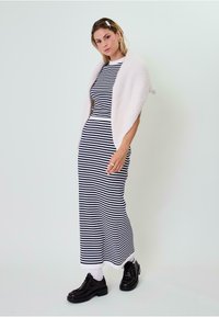 Prugasta maksi haljina u mornarsko plavoj i bijeloj boji od pamuka s uskim krojem, upotpunjena mekanim bijelim šalom. Crne čipkaste cipele i bijele čarape.