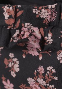 Zwarte stof met een bloemprint in roze en bruin, met een gerimpelde tailleband. De textuur lijkt zacht en elastisch.