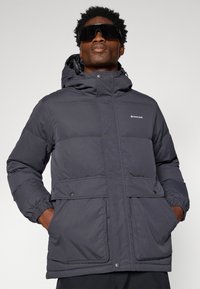 Puffer jacket in dark gray, featuring a hood, two front pockets with snap closures, elastic cuffs, and a subtle logo on the chest.