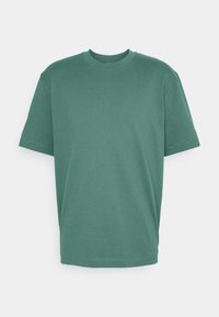 T-shirt en coton vert à manches courtes, encolure ronde et coupe décontractée. Pas de motifs ni de matériel visible. Texture lisse.