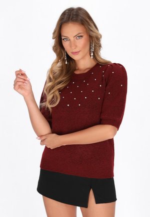 Pulover tricotat de culoare burgundă, cu mâneci scurte tip puff, decorat cu mărgele argintii pe față, asortat cu o fustă mini neagră.