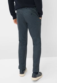 Pantaloni grigi scuri con una superficie liscia e cintura elastica, dotati di tasche posteriori con chiusura a bottone. Indossati con sneaker scuri.