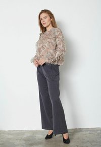 Průhledná béžová halenka s volánkovou texturou, těsně padnoucí v pase, doplněná tmavě šedými, širokými kalhotami a černými vysokými podpatky.