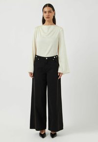 Krämfärgad blus med textur och breda ärmar, tillsammans med high-waisted svarta vida byxor med knappstängning och subtila detaljer.