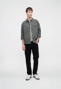 Camisa a cuadros en gris y negro con botones al frente, combinada con una camiseta verde clara, pantalones negros y zapatillas blancas con detalles grises.
