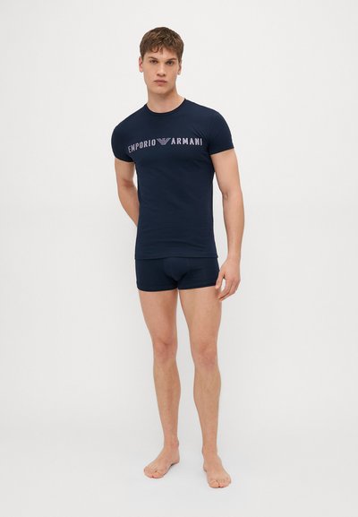 T-shirt ajustado azul-marinho com um logótipo, combinado com calções escuros. Tecido confortável com um design simples, sem padrões, e mangas curtas.