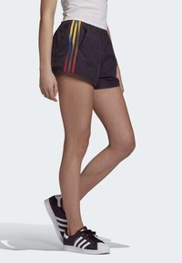 Černé sportovní šortky s duhovým pruhem po straně, s volným střihem. Kombinovány s černobílými teniskami.