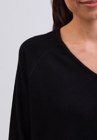 Czarny sweter z dzianiny z dekoltem w serek, z raglanowymi rękawami i miękką teksturą. Zbliżenie podkreśla szczegóły dekoltu i materiału.