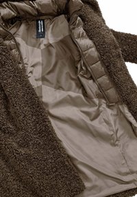 Bruine gestructureerde jas met een fluffy buitenmateriaal en een gladde binnenvoering. Voorzien van een ritsluiting en een label aan de binnenzijde.