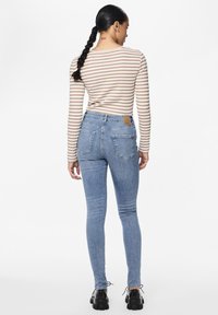 Gestreepte longsleeve top in beige en crème, gecombineerd met lichtblauwe skinny jeans. Opvallende details zijn de achterzakken en een leren patch op de tailleband.