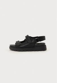 Sandalias de cuero negro con una suela gruesa, correas ajustables y detalles troquelados para una mejor transpirabilidad. Textura suave con un acabado mate.