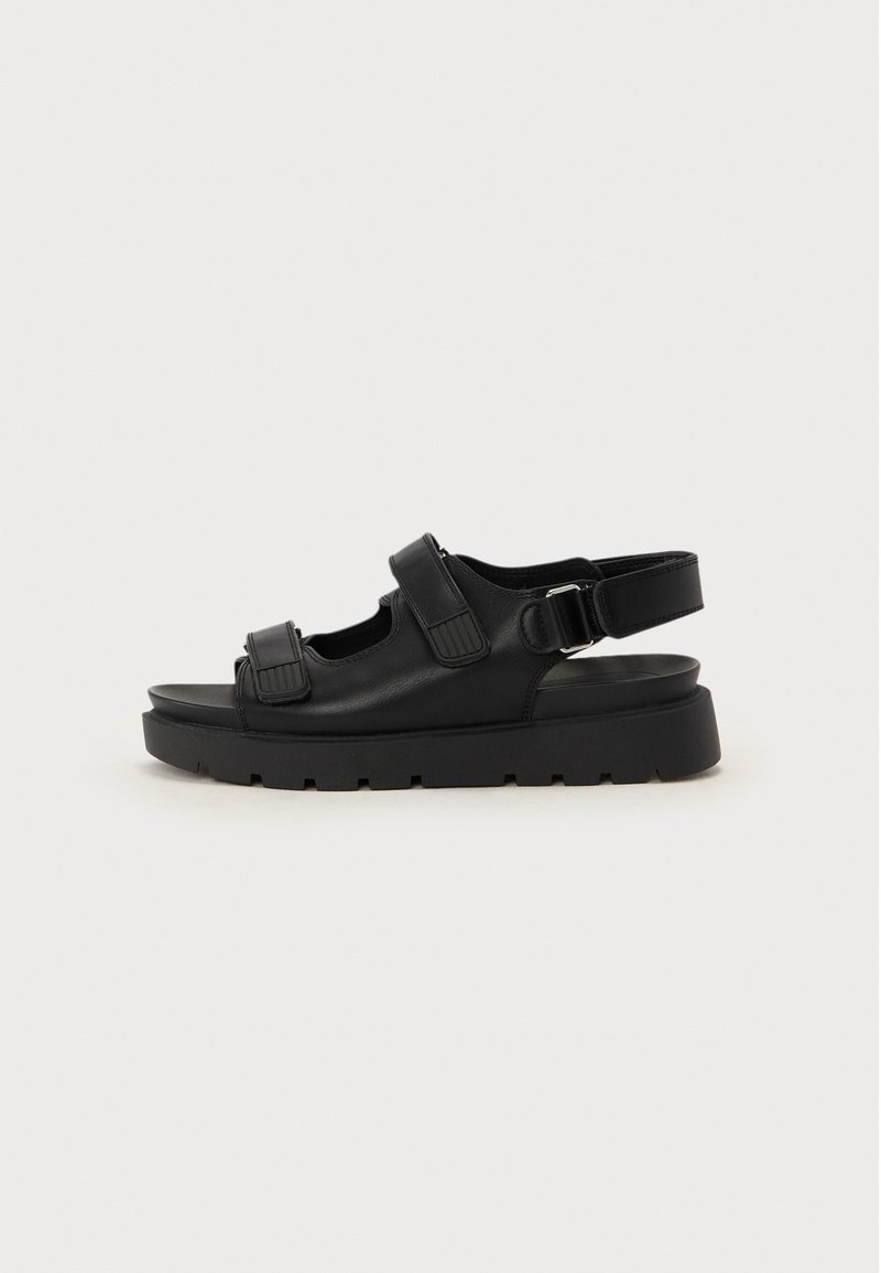 Sandalias de cuero negro con una suela gruesa, correas ajustables y detalles troquelados para una mejor transpirabilidad. Textura suave con un acabado mate.
