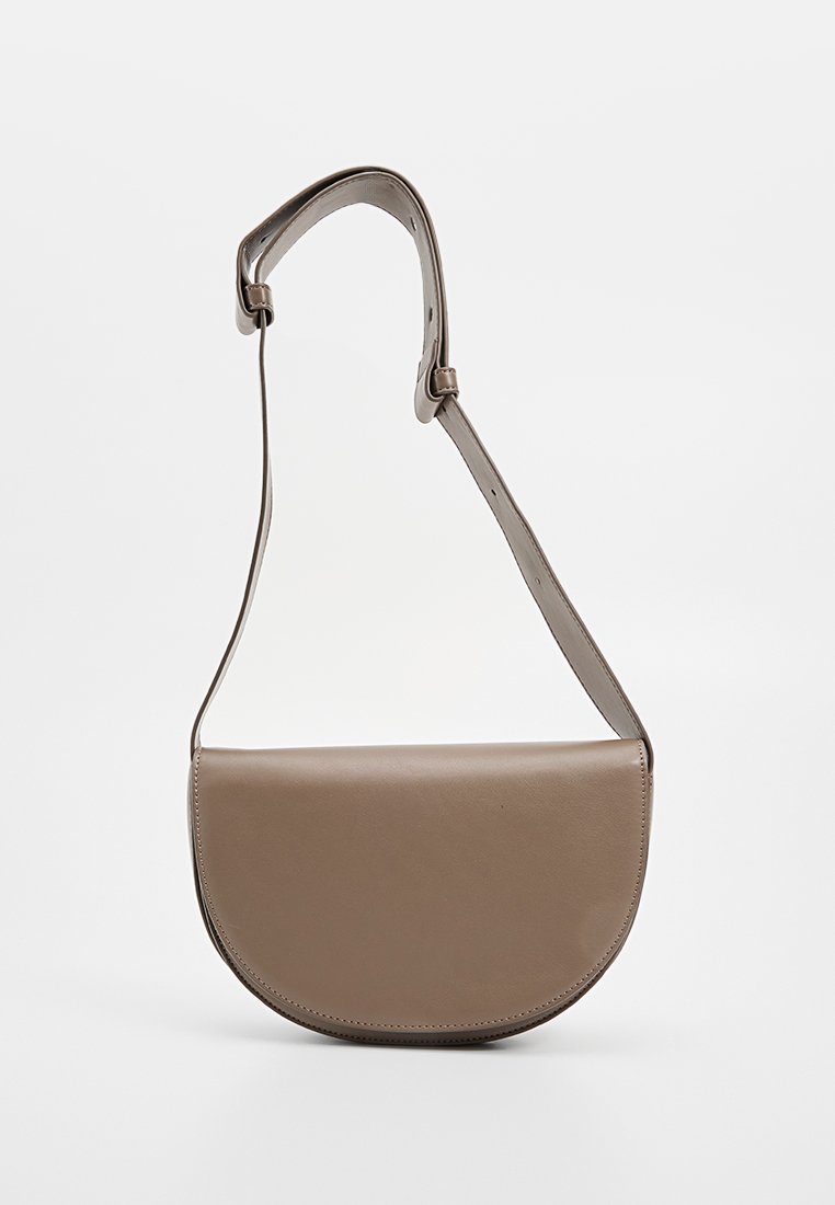 Bolso de cuero beige tipo bandolera con solapa redondeada, correa ajustable y textura suave. Diseño minimalista sin herrajes visibles.