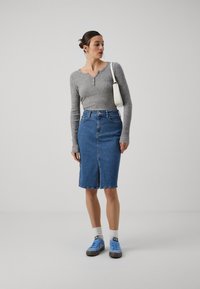 Haut gris à manches longues côtelé avec un col à boutons, associé à une jupe crayon en denim avec une fente devant, et des baskets bleues.