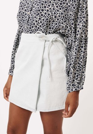 Jupe portefeuille bleu clair en tissu doux, dotée d'une ceinture à nouer à la taille et d'un ourlet net, associée à un chemisier à motifs floraux.