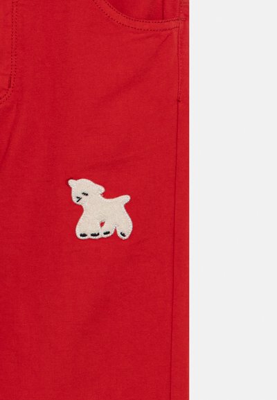 Κόκκινο ύφασμα με ένα μικρό λευκό κεντημένο αρνάκι κοντά στη ραφή μιας τσέπης σε ρούχο.