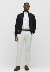 Marinblå zip-up tröja, vit skjorta med knappar, beige byxor, bruna skor. Släta texturer och figurnära design med en klassisk färgpalett.