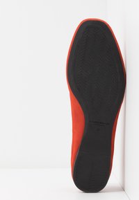 Semelle d'une chaussure plate en daim rouge avec semelle en caoutchouc noire, taille 37, photographiée à la verticale contre un fond blanc d'angle.