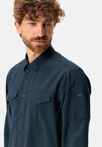 Camicia button-up blu navy scuro realizzata in tessuto leggero; presenta due tasche sul petto e un logo sul maniche.