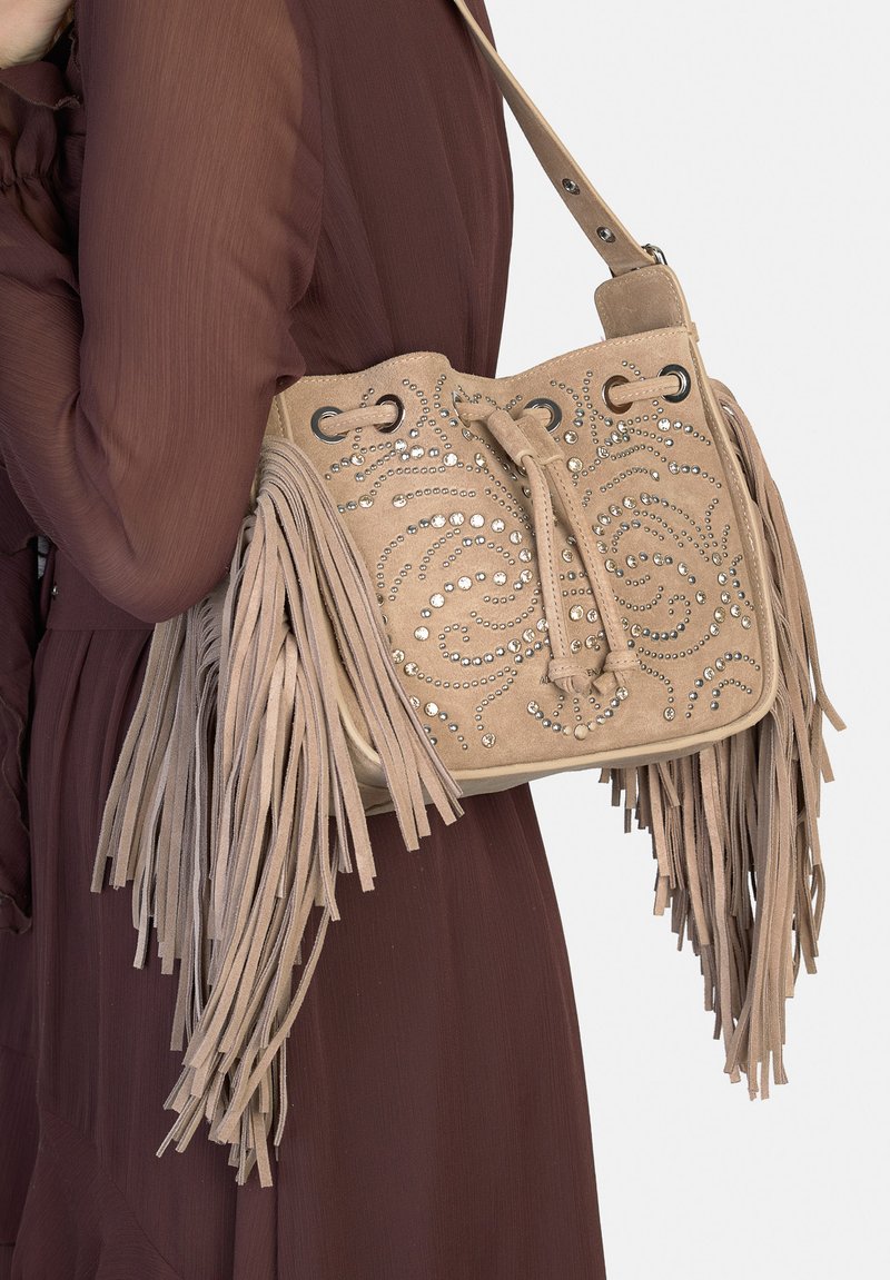 Borsa a secchiello in camoscio beige con lunghe frange, impreziosita da borchie d'argento disposte a motivi a spirale, e tracolla regolabile.