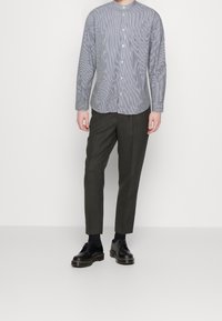 Gestreepte overhemdbloes in blauw en wit, met een mandarin kraag, gecombineerd met donkergrijze op maat gemaakte broek en zwarte veterschoenen.