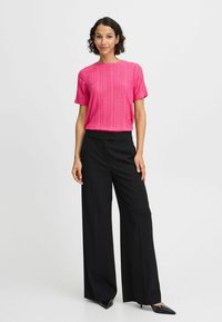 Rosa kurzärmliges Oberteil mit einem strukturierten Muster, kombiniert mit schwarzen weiten Hosen und spitzen schwarzen Absätzen. Einfaches, klares Design.