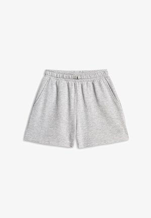 Jeune fille aux longs cheveux bruns portant un sweat-shirt rose et un short gris, portant un sac violet et écoutant de la musique avec des écouteurs.
