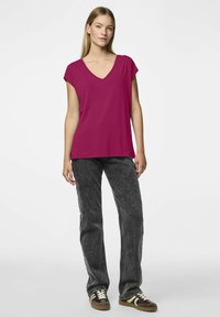 Fuksjowa koszulka z dekoltem w kształcie litery V i krótkimi rękawkami, w zestawieniu z szarymi dżinsami i brązowymi trampkami. Gładka faktura, luźny krój.
