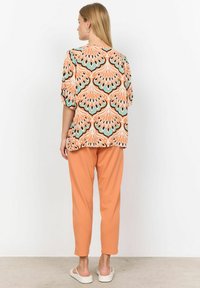 Løs siddende bluse med orange og teal blomstermønster, parret med matchende løse bukser. Blødt stof, afslappet design og ensfarvede manchetter.