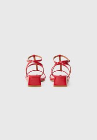 Red patent leather sandals with a square heel, adjustable ankle straps, and an open toe design. Smooth texture with minimal hardware accents.