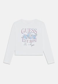 Weißes langärmliges Cropped-Top mit floralem Grafikdesign, das blaue Blumen und den Aufdruck "GUESS EST. 1981 Los Angeles" in mehrfarbigem Druck zeigt.