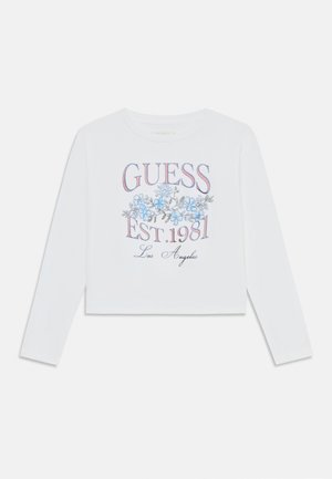 White long-sleeve crop top featuring floral graphic design with blue flowers and text "GUESS EST. 1981 Los Angeles" in multicolored print.