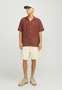 Camisa de punto abierto de color óxido, de manga corta y con botones, combinada con pantalones cortos de pana color crema hasta la rodilla y zapatos beige.