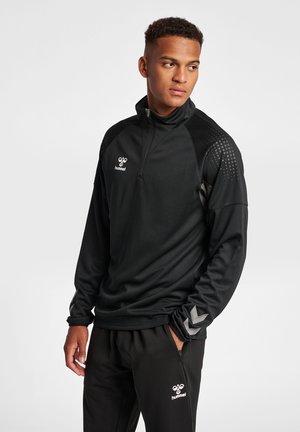 Maglietta nera sportiva a mezza zip con tessuto testurizzato, dettagli argentati e logo; abbinata a pantaloni neri con logo coordinato.