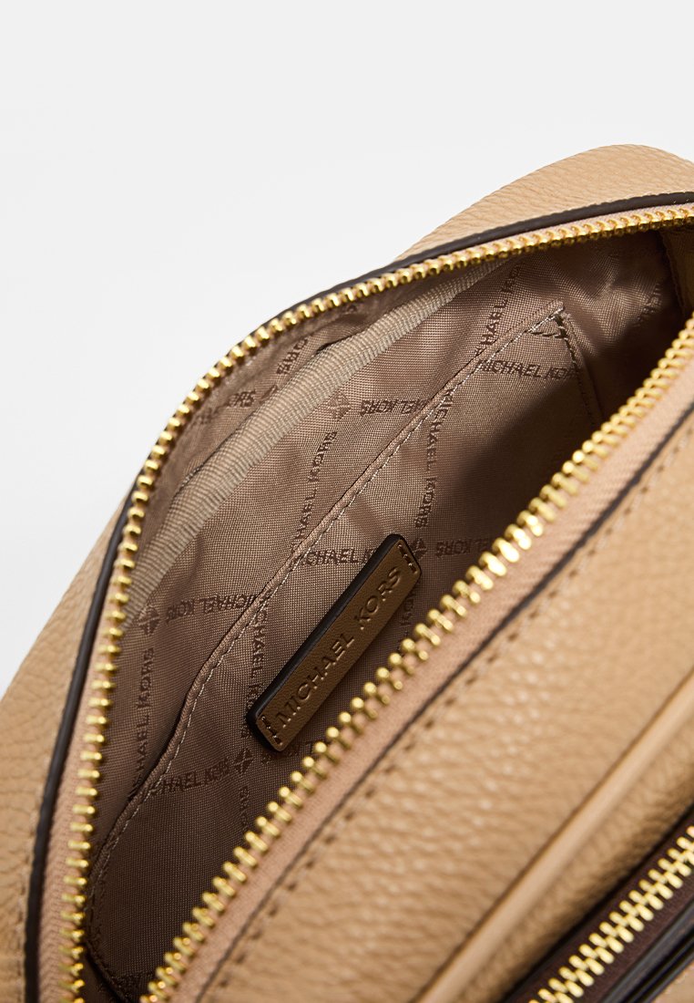 Interior de un bolso de cuero marrón con cremallera dorada, que cuenta con un forro de satén suave y un parche con la marca. Contiene un bolsillo separado y un patrón de logo.